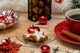 Alt-text: Holiday cookies on a small plate beside a cup of coffee and cinnamon stick on a festive table setting
