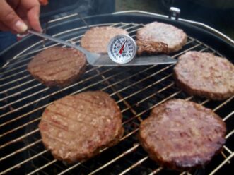 Checking the temperature with a thermometer while grilling hamburgers on a charcoal grill.
