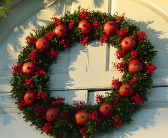 A traditional boxwood wreath is decorated with pomegranates and nandina berries.