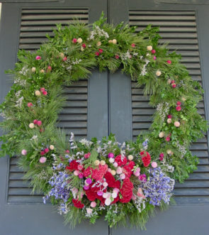 Dried flowers such as lavender, cock’s comb, baby’s breath, and gomphrena, brighten up an evergreen wreath made of pine and boxwood.
