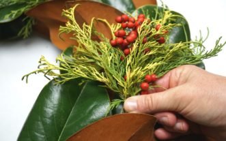 For contrast, use brightly colored conifer foliage and holly berries. Make the bundle and tuck it between the magnolia leaves, securing it with a fern pin. 