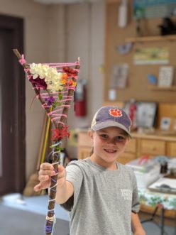A camper weaving a “Y” stick with yarn and flowers.