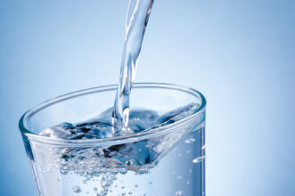Clear water being poured into a glass against a light blue background.