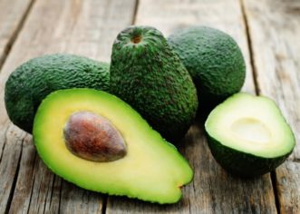 Sliced avocado with the pit in front of whole avocados
