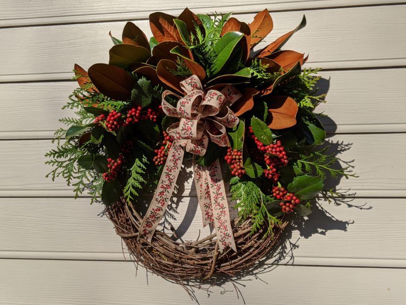 A grapevine wreath decorated with magnolia, arborvitae, and holly berries adds a festive touch near the front door.