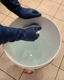 Scrubbing a fermenter bucket with a clean brush and dilute PBW solution.