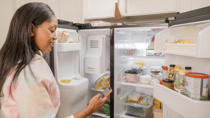A woman holding a cellphone in front a refrigerator.