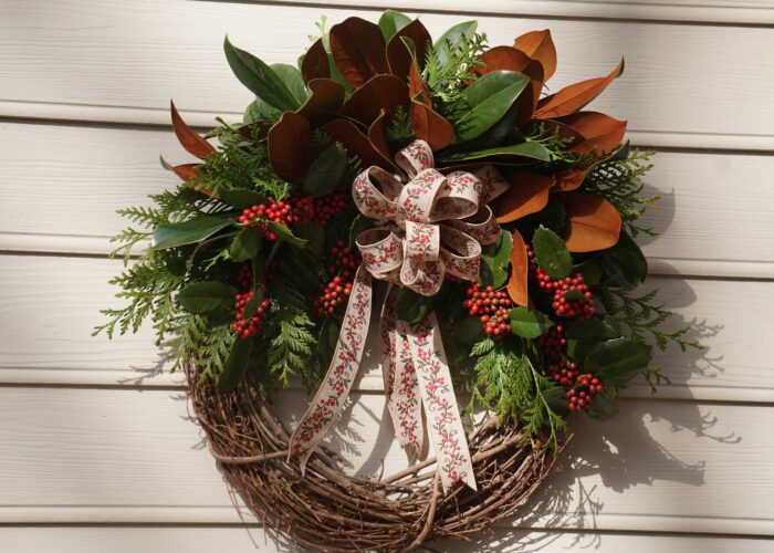A grapevine wreath is decorated with Green Giant arborvitae foliage, magnolia leaves, and holly to brighten the holiday season.
