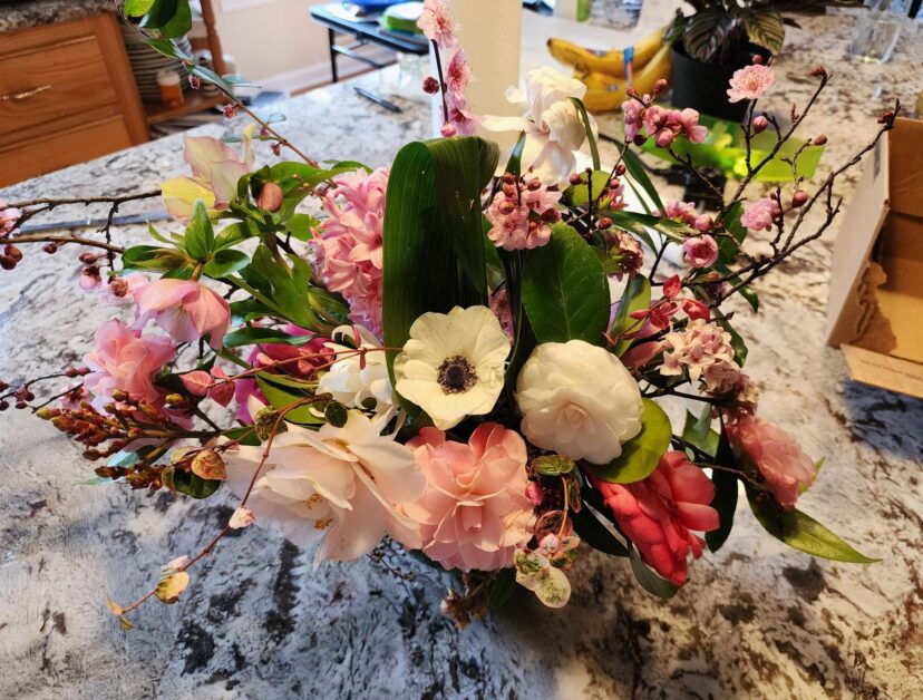 Early spring floral arrangement of flowering apricot, camellias, Lenten rose, and anemone.