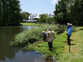 A group of people standing near a pond Description automatically generated