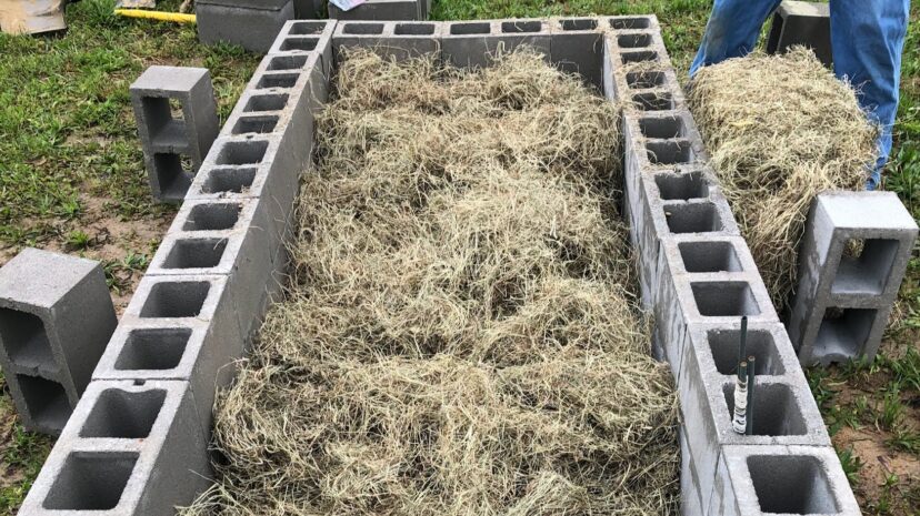 Straw and grass clippings are added on top of the leaf litter layer in a raised garden bed.