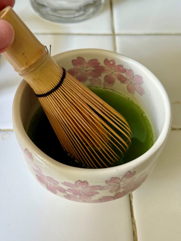 Matcha whisk beside a bowl of green matcha powder