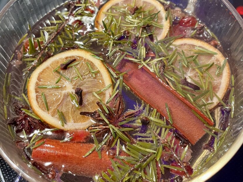Simmer pot with cinnamon sticks, orange slices, cedar sprigs, and whole spices gently steaming on a stovetop.