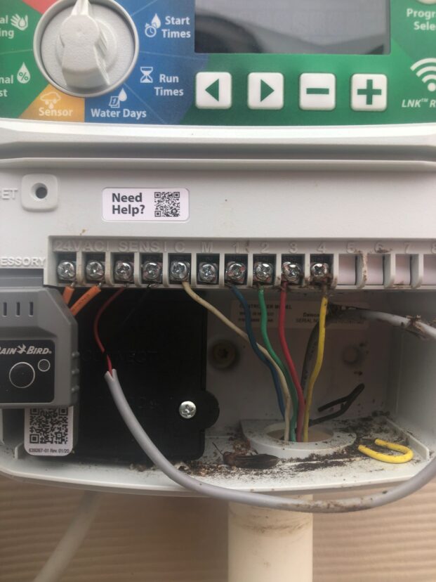 Close-up of an irrigation controller with wiring terminals and color-coded zone wires connected inside the control panel.