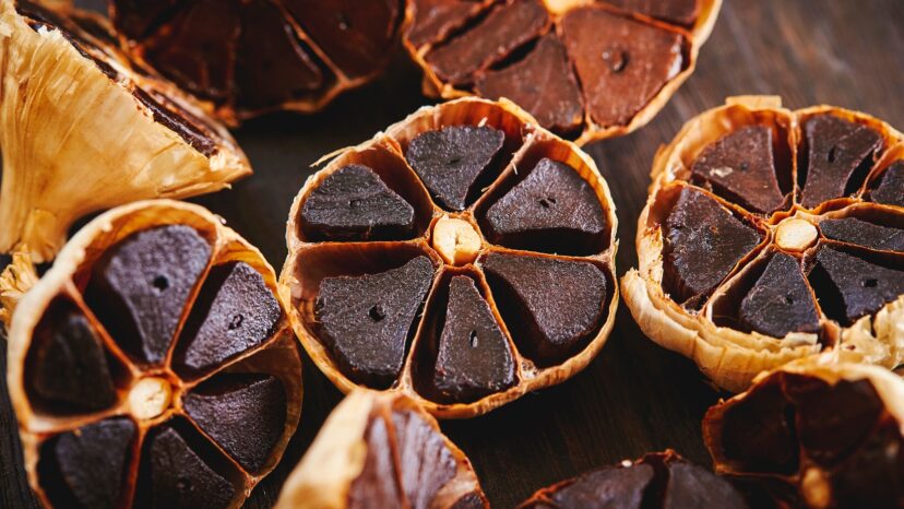 A bulb of black garlic with dark, soft cloves showing the aged color and texture.