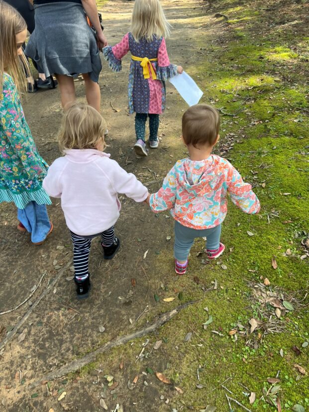Children walking together on a wooded trail, holding hands while exploring outdoors