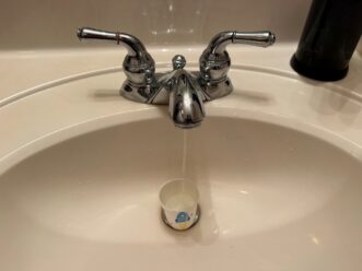Measuring faucet drip rate using a 3-ounce bathroom cup to determine gallons per hour flow in a sink.