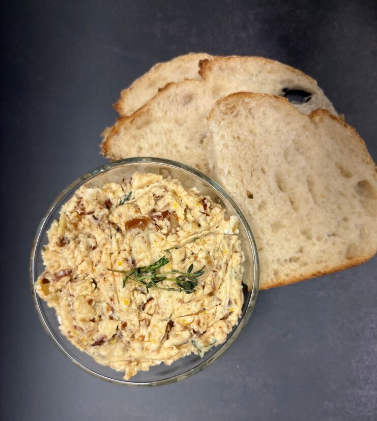 Creamy feta spread with chopped dates and herbs in a bowl, served alongside slices of crusty bread.
