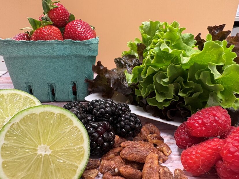 Strawberries, raspberries, blackberries, leafy greens, lime halves, and candied nuts arranged on a surface.