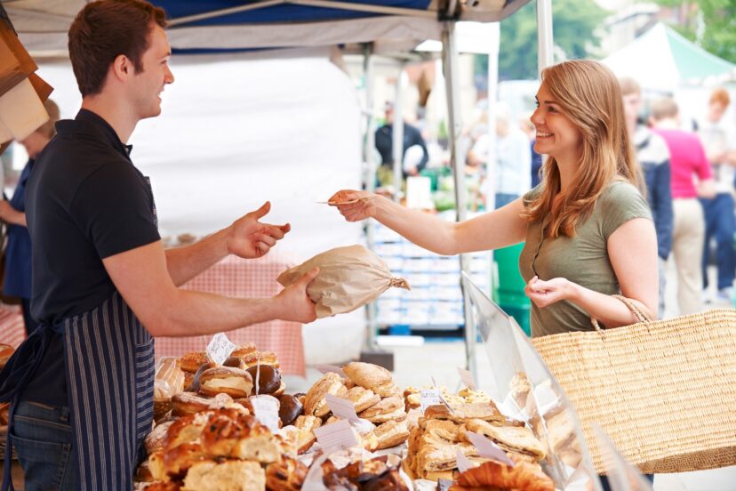 "Vendor displaying labeled baked goods under a covered tent at a South Carolina farmers market while keeping products protected from dust and sunlight."