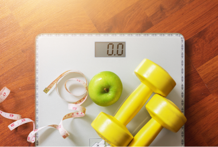 A bathroom scale, green apple, measuring tape, and yellow hand weights illustrate health beyond body weight.