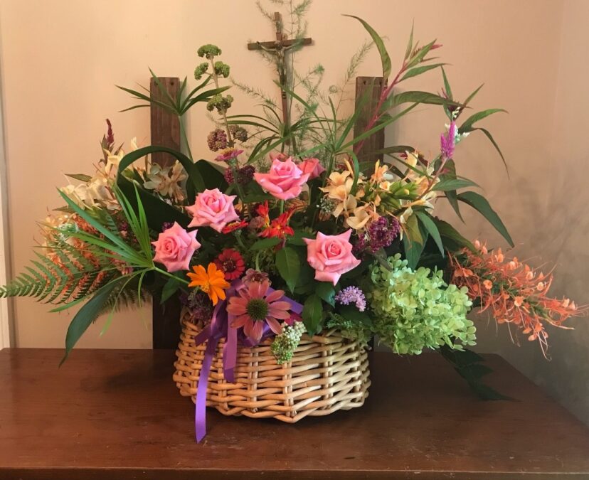 Colorful late-summer flower arrangement with pink roses, orange and purple flowers, greenery, and ornamental grasses in a woven basket