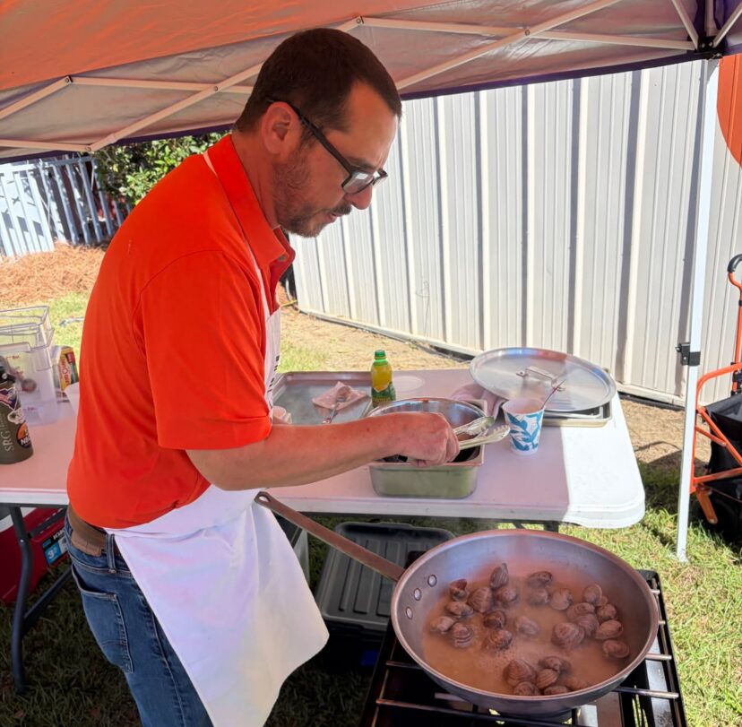 A Clemson Extension agent prepares clams in a pan at an outdoor event.