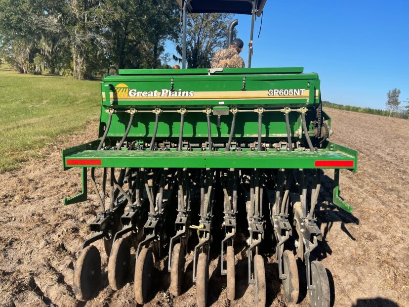 A tractor-mounted seed drill plants a cover crop in a freshly prepared field.