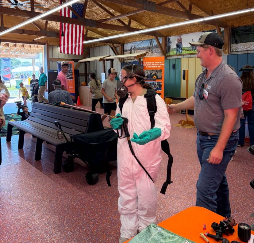Extension staff demonstrate pesticide protective equipment at an agricultural event.